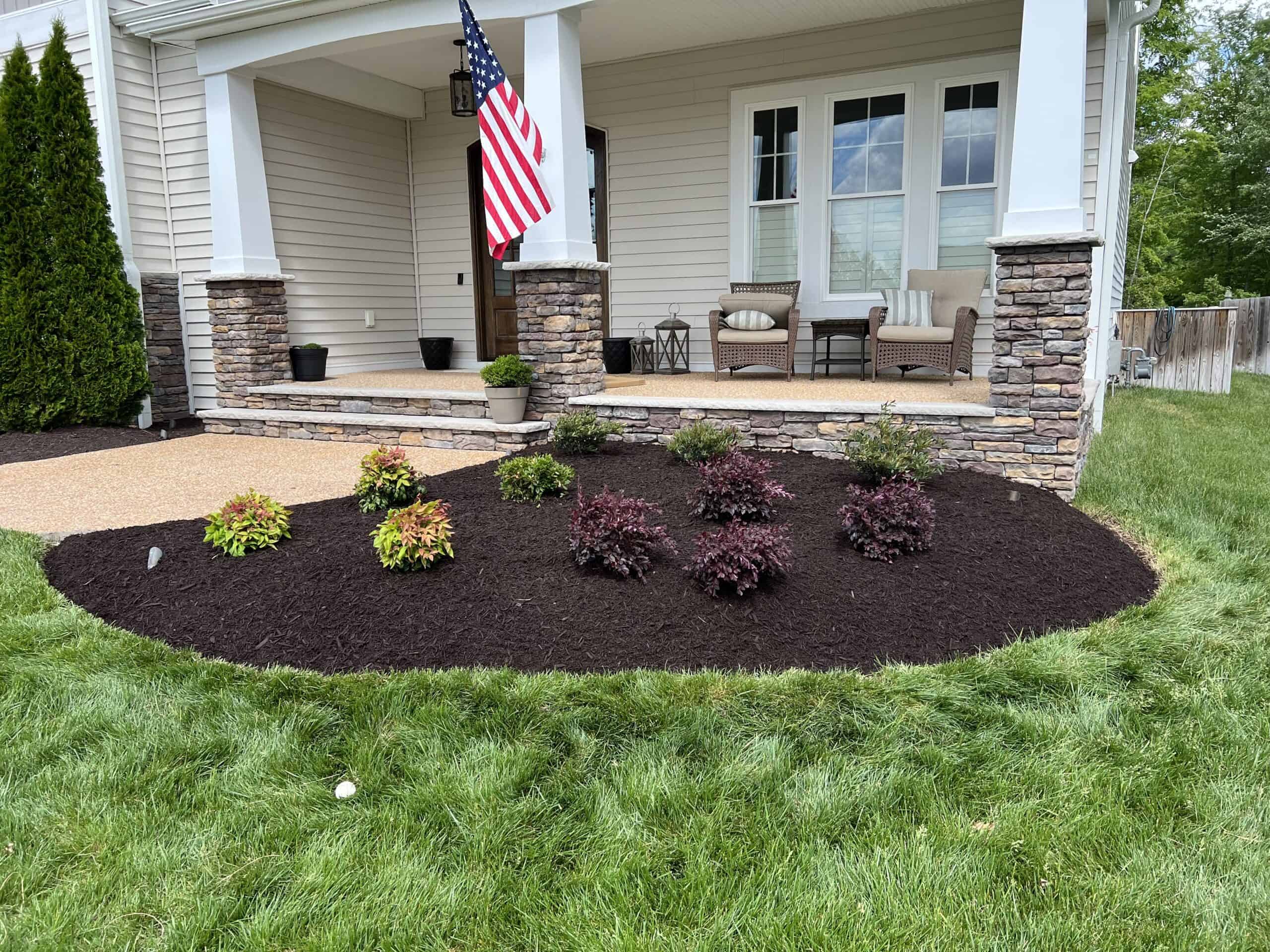 a heaped mulch bed with seasonal plants scattered throughout in front of a traditional-style home